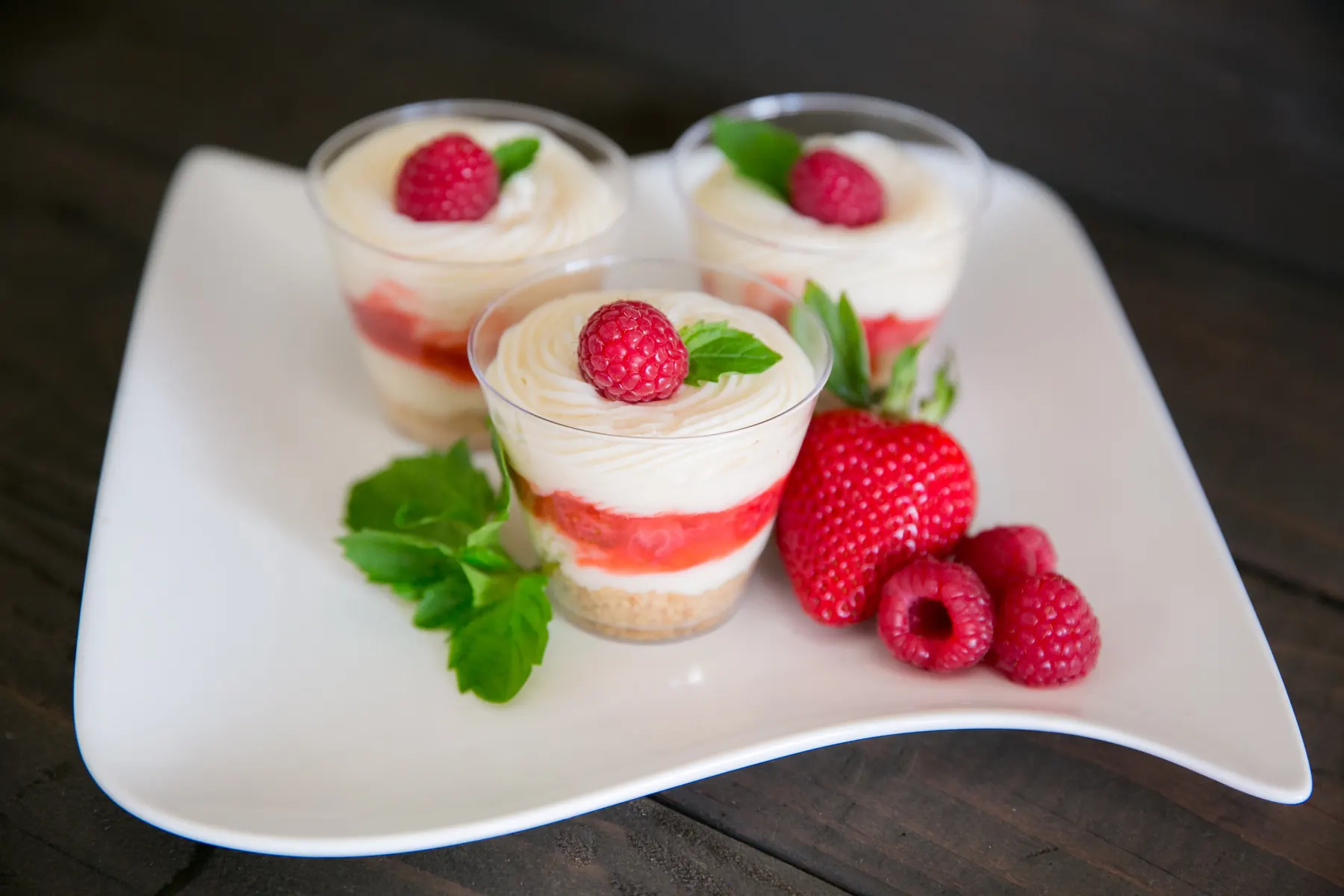 Layered berry cheesecake dessert cups topped with fresh raspberries